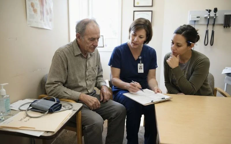 A senior care advisor sitting with an older adult and a family member, walking through a level of care assessment checklist on a clipboard
