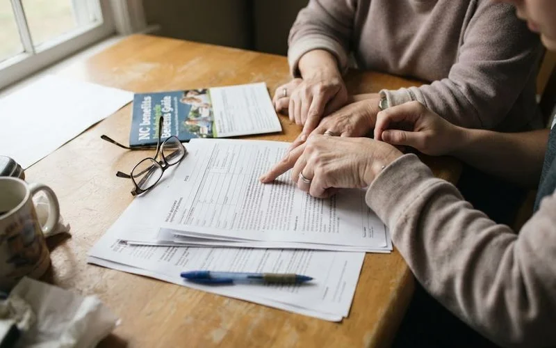 A family member reviewing paperwork with a senior living advisor at a table, discussing Medicaid and payment options for assisted living care